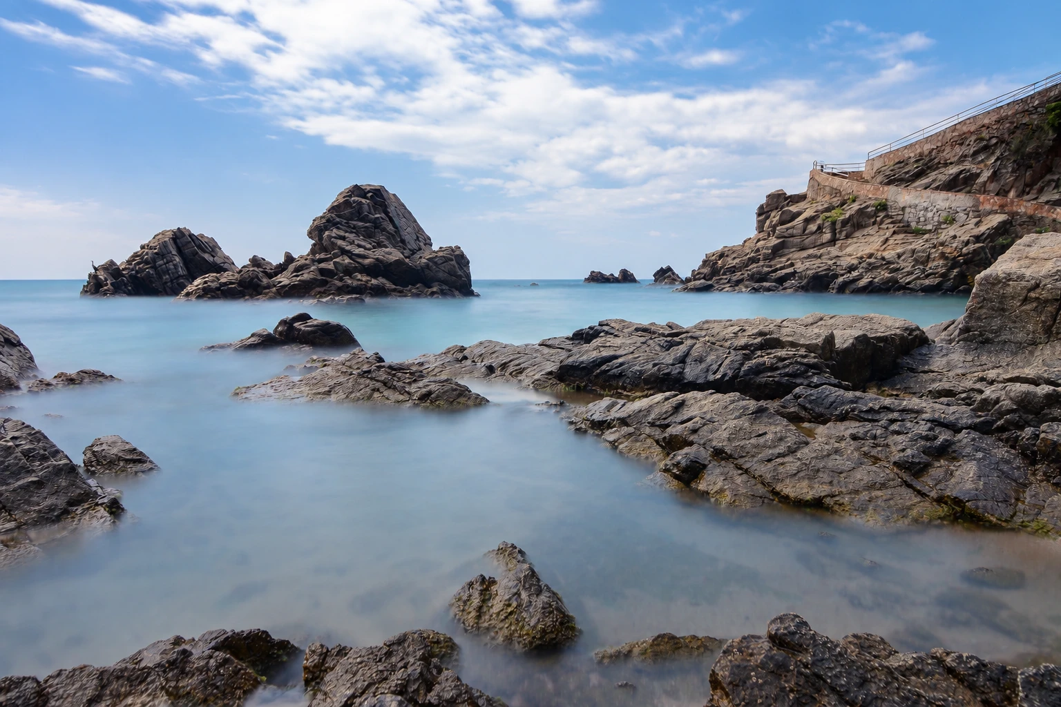 Острая скала в гладкой молочной воде, впереди тёмные камни